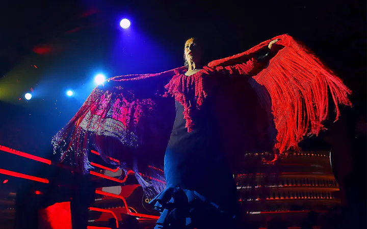 Flamenco dancer performing under stage lights with red shawl, Spain.