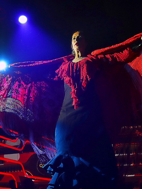 Flamenco dancer performing under stage lights with red shawl, Spain.
