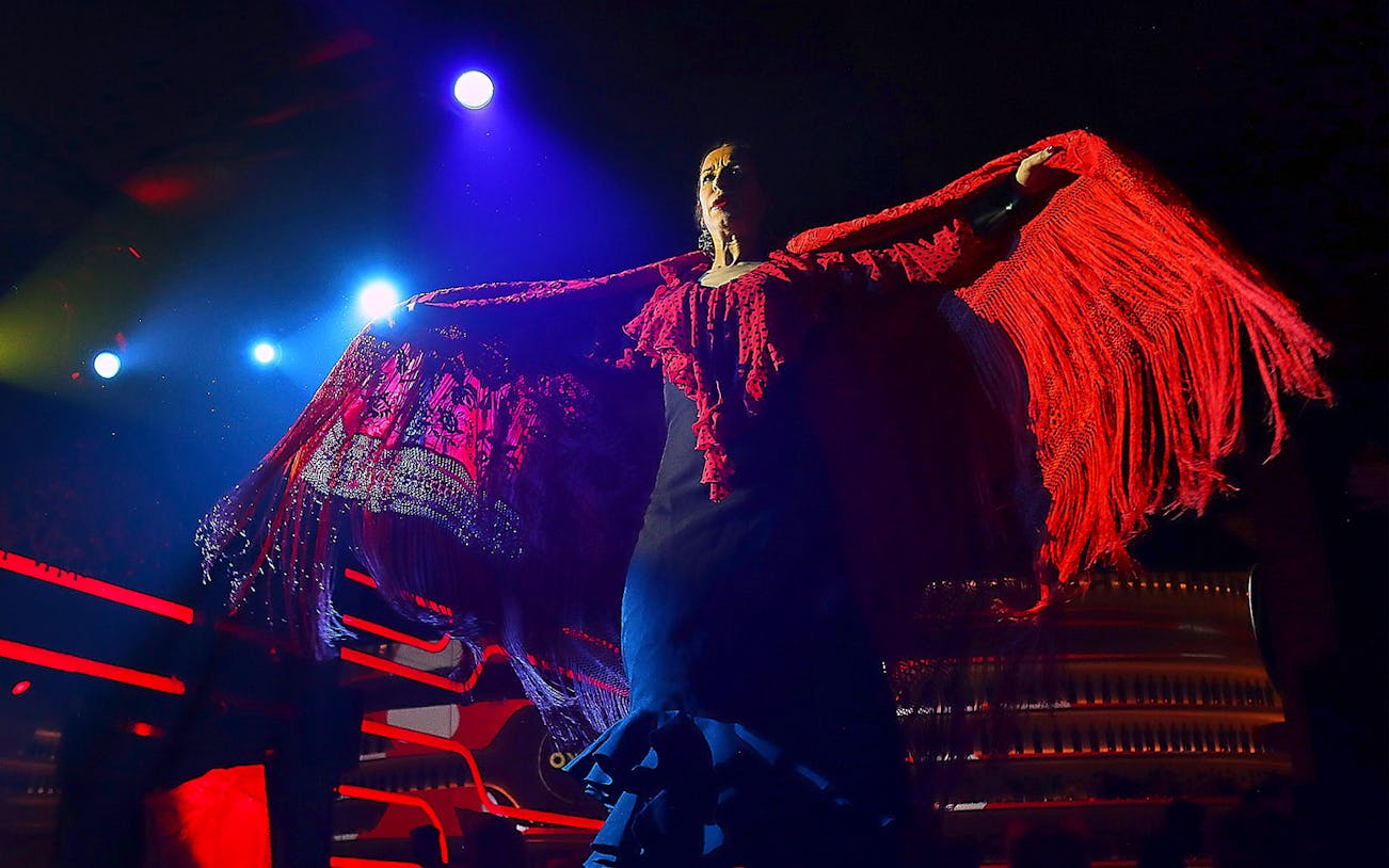 Flamenco dancer performing under stage lights with red shawl, Spain.