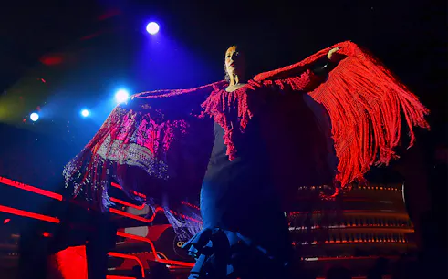 Flamenco dancer performing under stage lights with red shawl, Spain.