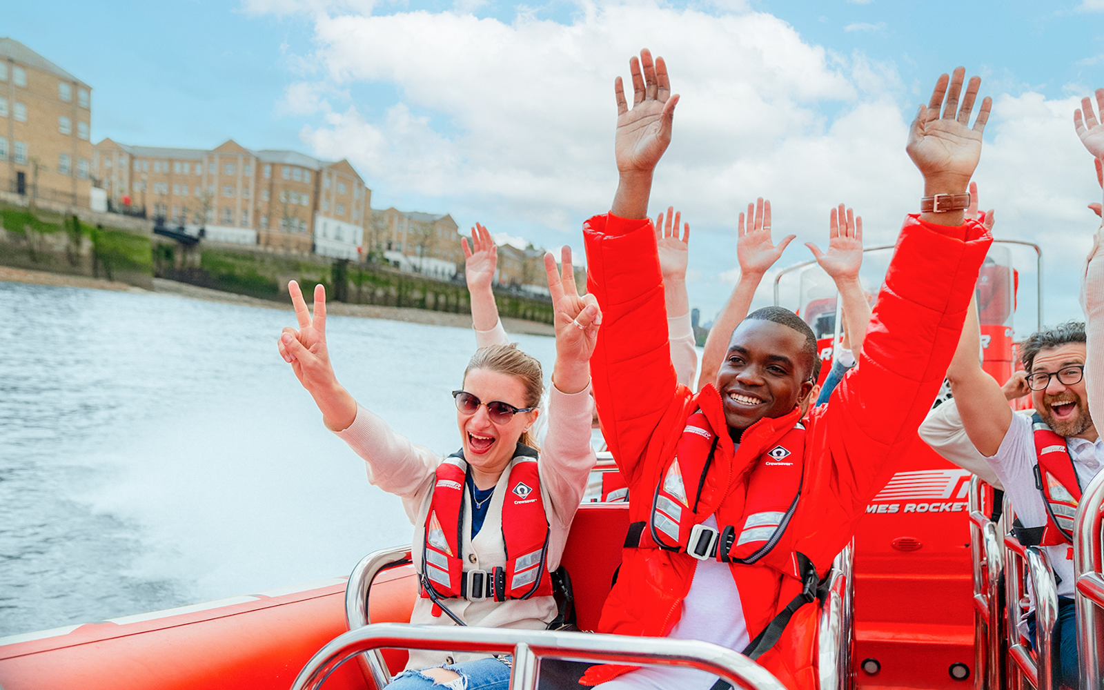 People enjoying a Thames speed boat ride in London, raising hands and smiling.