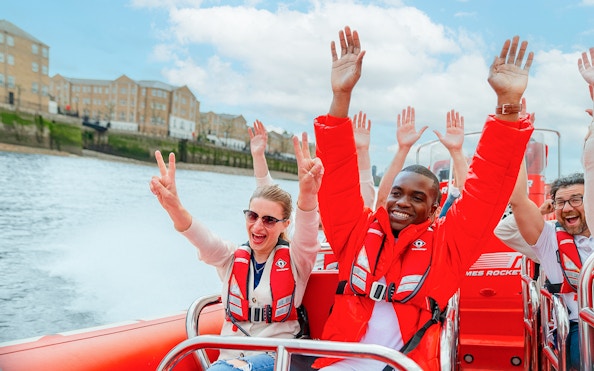 People enjoying a Thames speed boat ride in London, raising hands and smiling.
