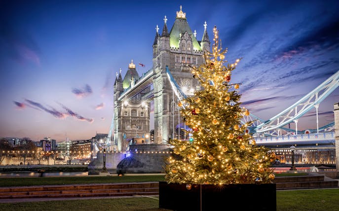 Tower Bridge in London with a decorated Christmas tree in the foreground.