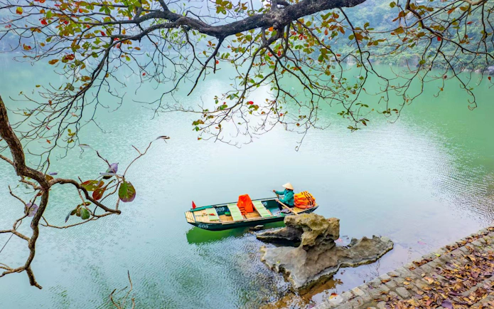 Boat on river at Trang An Landscape Complex, Vietnam, with limestone rocks and overhanging branches.