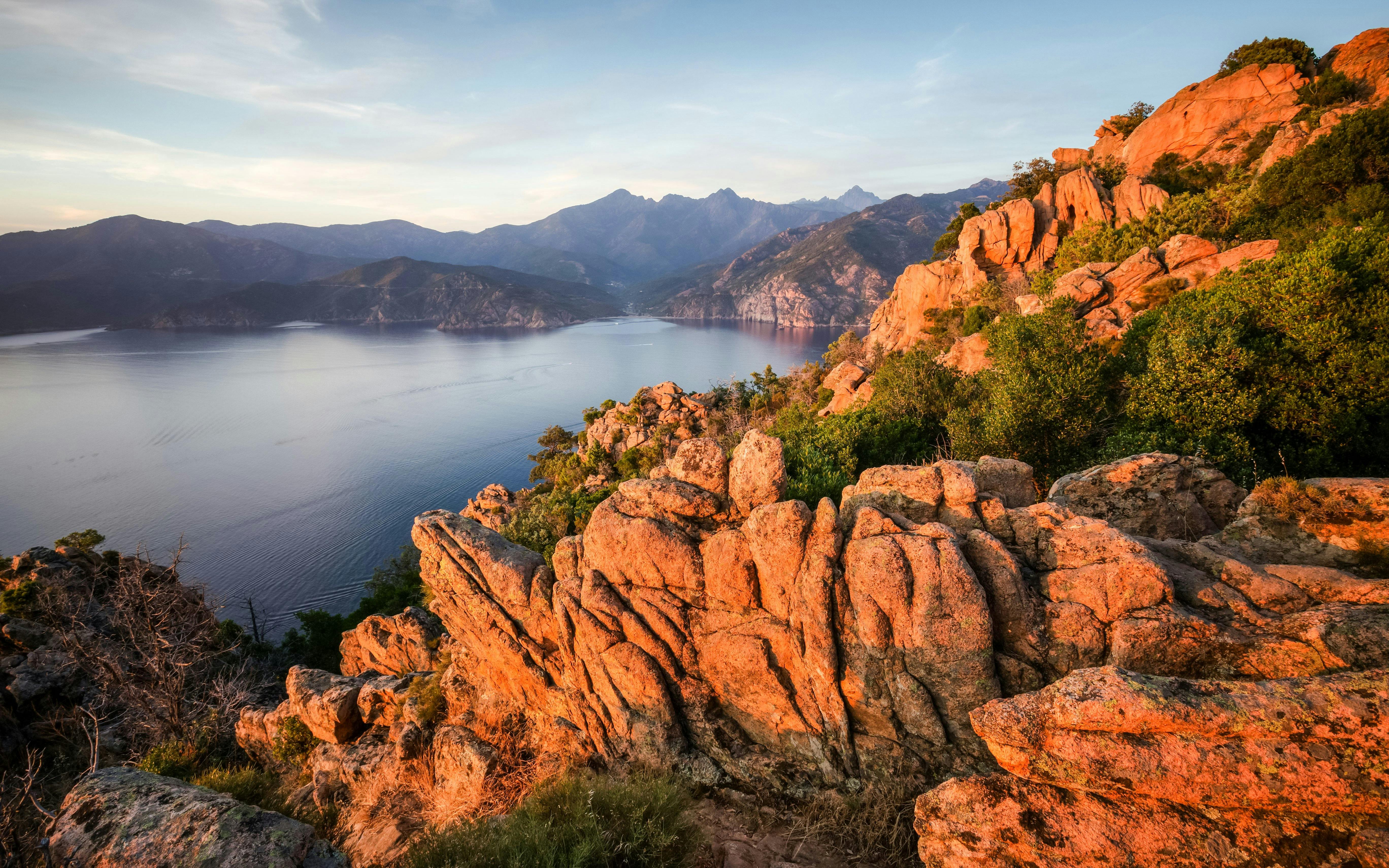 Rocky coastline at sunset near Marseille, overlooking calm sea and distant mountains.