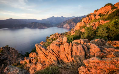 Rocky coastline at sunset near Marseille, overlooking calm sea and distant mountains.