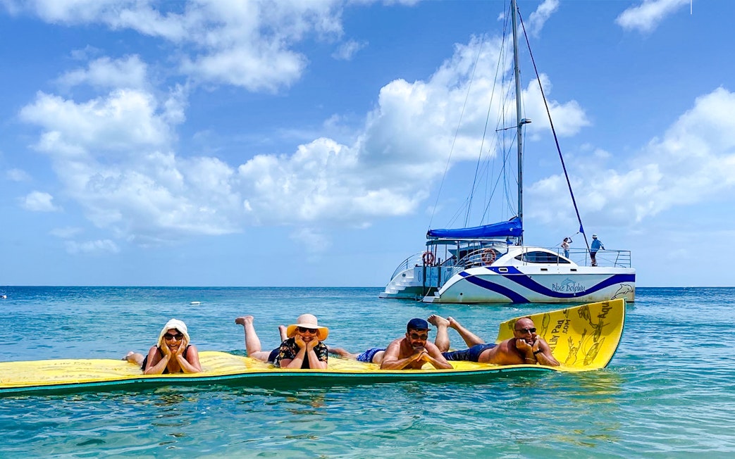 People relaxing on a floating mat near a sailboat during a dolphin eco cruise, Fraser Island, K'gari.