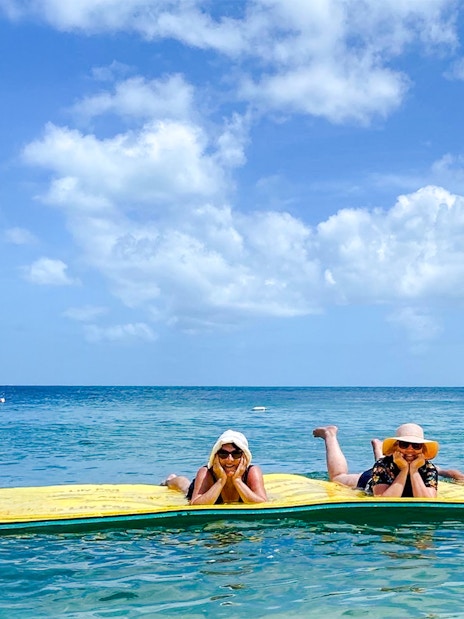 People relaxing on a floating mat near a sailboat during a dolphin eco cruise, Fraser Island, K'gari.
