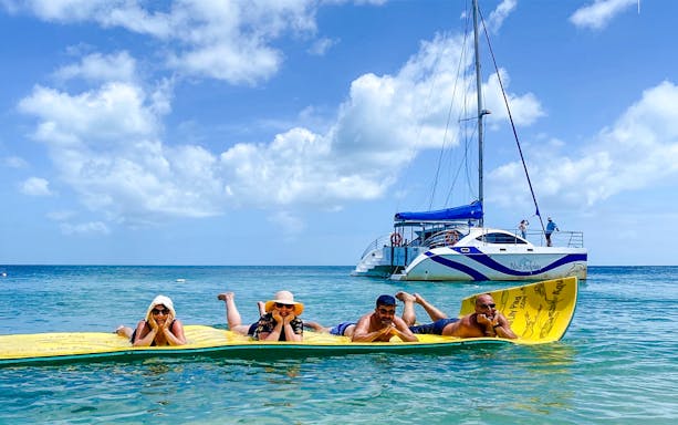 People relaxing on a floating mat near a sailboat during a dolphin eco cruise, Fraser Island, K'gari.