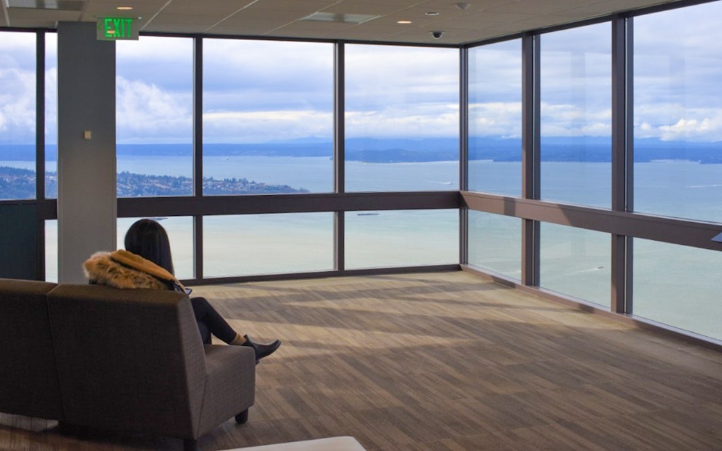 Person sitting in Sky View Observatory, Seattle, overlooking Puget Sound through large windows.