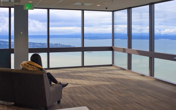 Person sitting in Sky View Observatory, Seattle, overlooking Puget Sound through large windows.