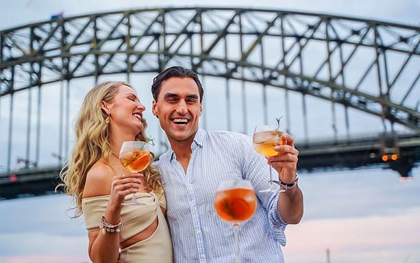 Couple enjoying drinks on a Christmas Day lunch cruise with Sydney Harbour Bridge in background.