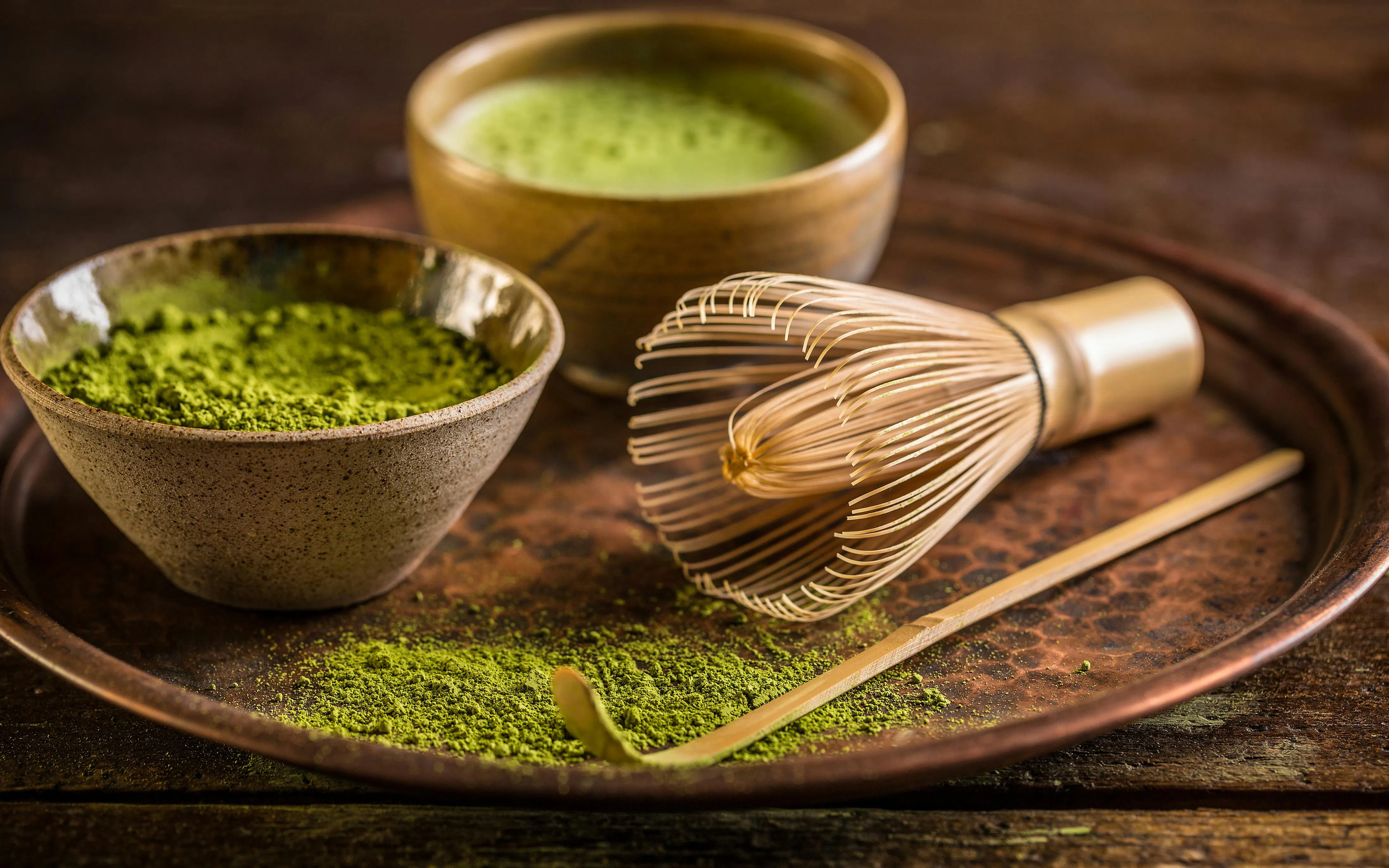 Matcha tea powder with bamboo whisk and bowl on a tray.