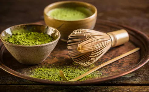 Matcha tea powder with bamboo whisk and bowl on a tray.