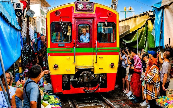 Train passing through Maeklong Train Market in Bangkok, surrounded by vendors and tourists.