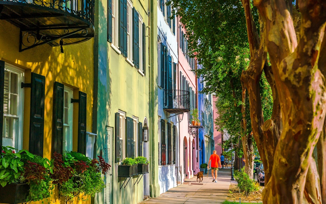 Colorful historic houses on Rainbow Row, Downtown Charleston, South Carolina, with a person walking a dog.