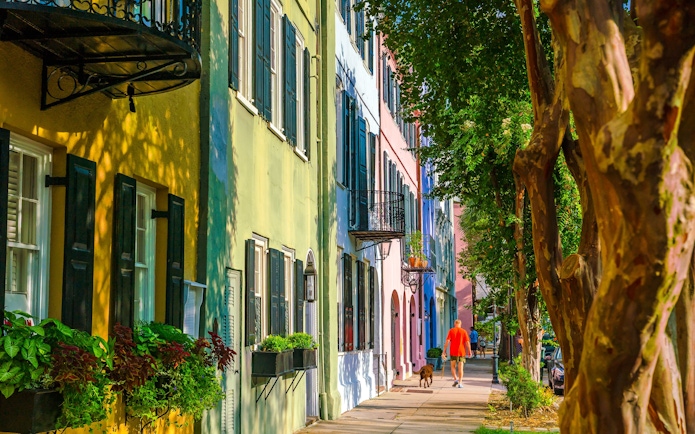 Colorful historic houses on Rainbow Row, Downtown Charleston, South Carolina, with a person walking a dog.