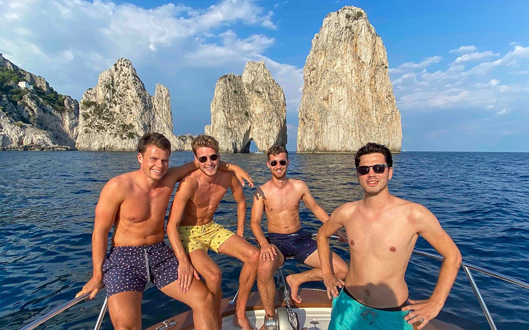 Boat tour near Faraglioni rocks, Capri, with group enjoying the view.