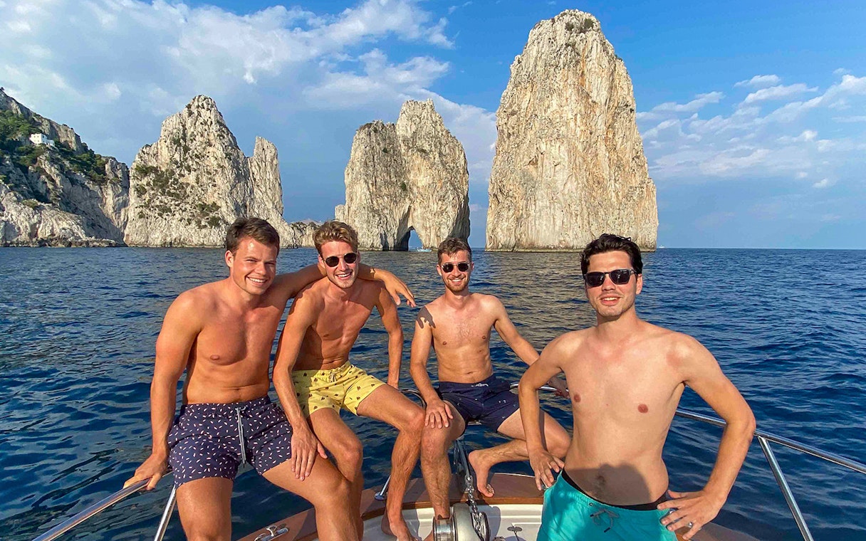Boat tour near Faraglioni rocks, Capri, with group enjoying the view.