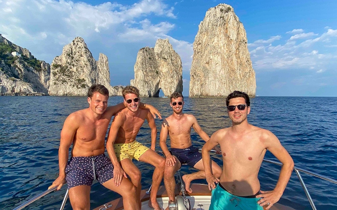 Boat tour near Faraglioni rocks, Capri, with group enjoying the view.