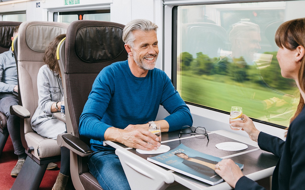 Travelers enjoying drinks in first-class seats on a Eurail train.