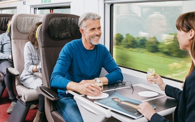 Travelers enjoying drinks in first-class seats on a Eurail train.