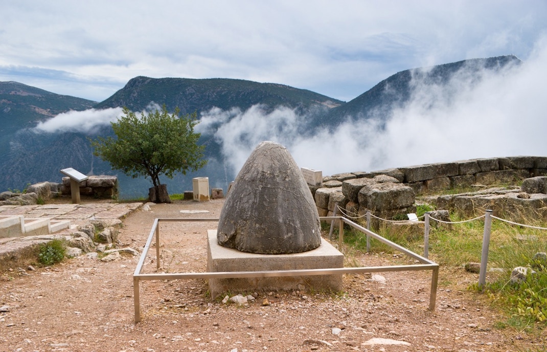 Omphalos stone at Delphi archaeological site with mountains in the background.