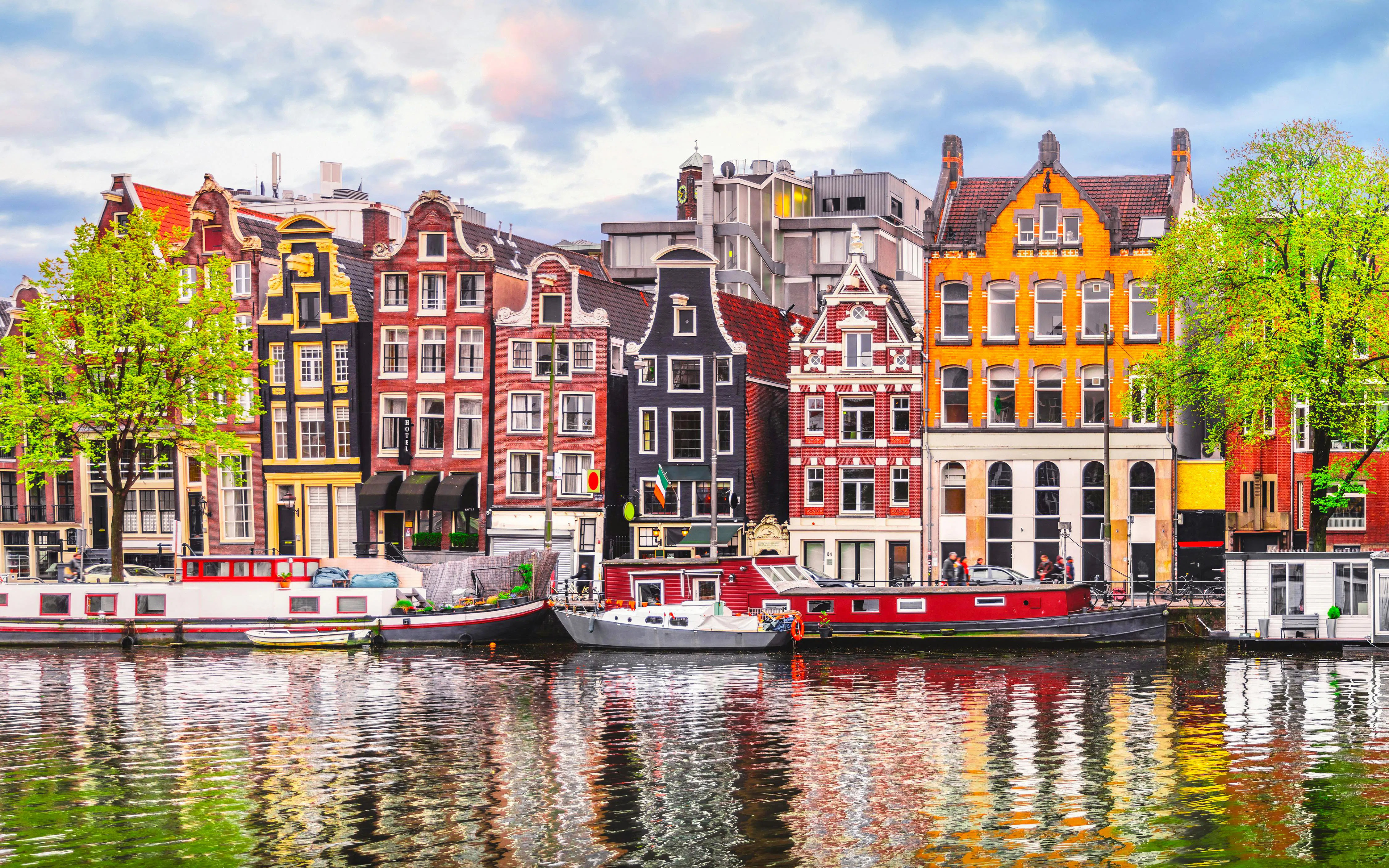 Dancing houses along Amsterdam canal with colorful facades and boats.