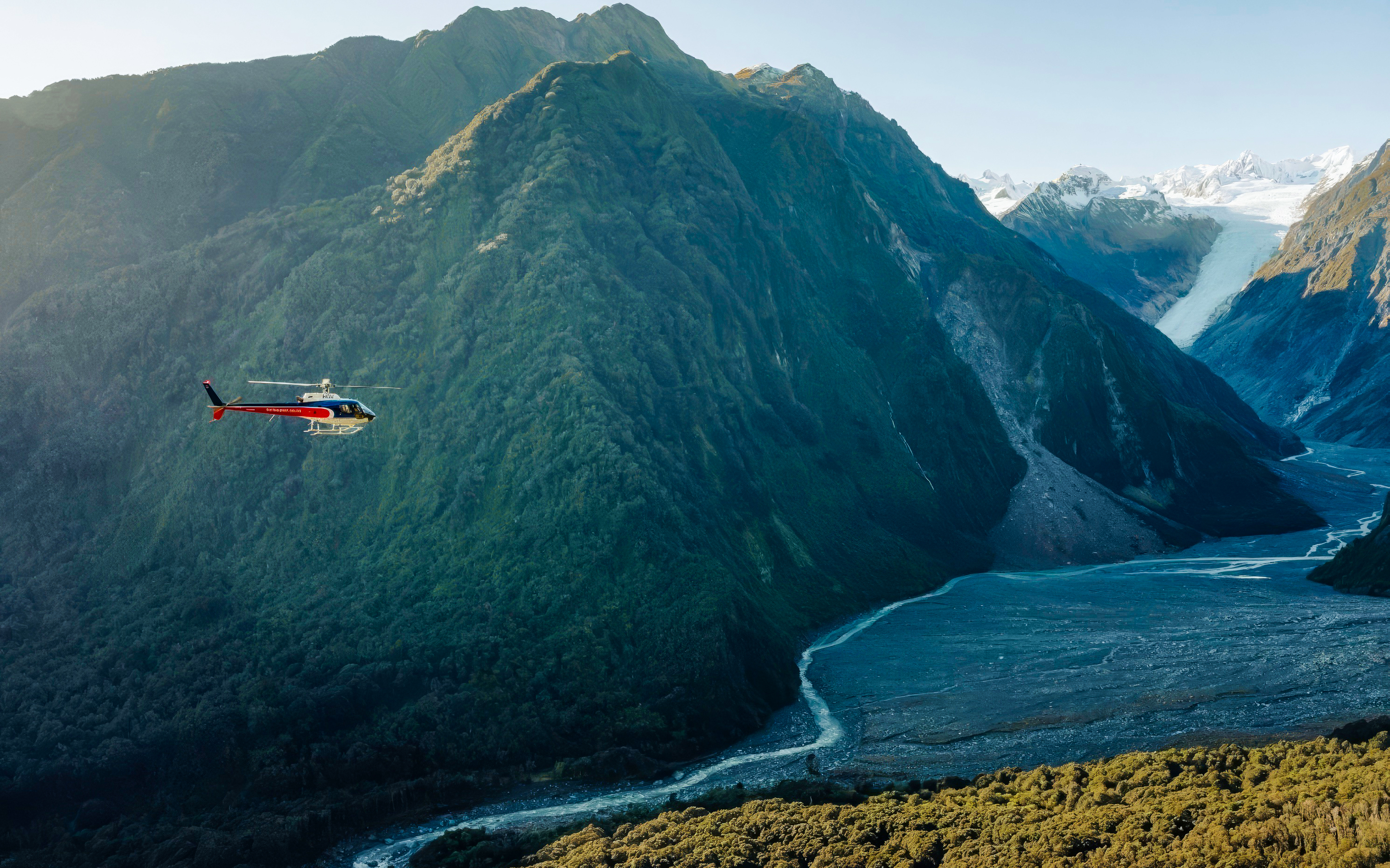Helicopter flying over Franz Josef Glacier in New Zealand with lush mountains.