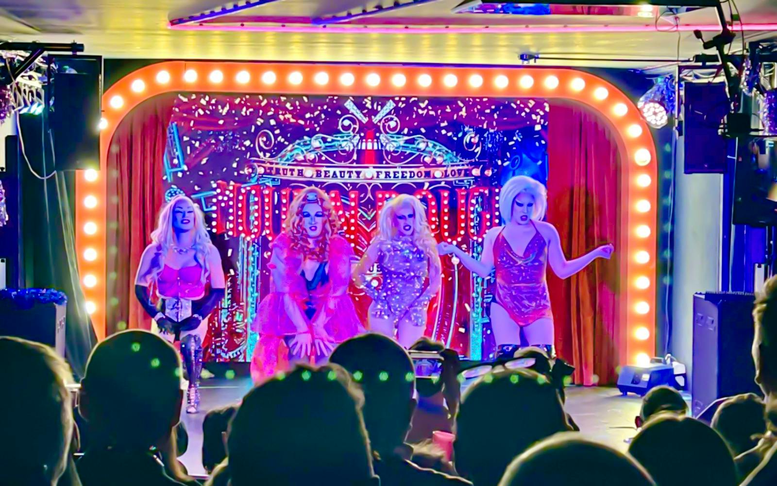 Drag performers on stage during the Drag Queen Hungary Show with vibrant lights and audience.