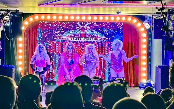 Drag performers on stage during the Drag Queen Hungary Show with vibrant lights and audience.