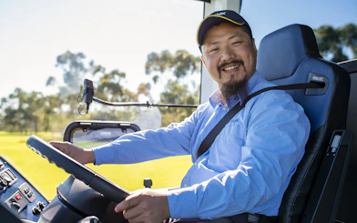 Bus driver smiling while steering through Adelaide Hills tour.