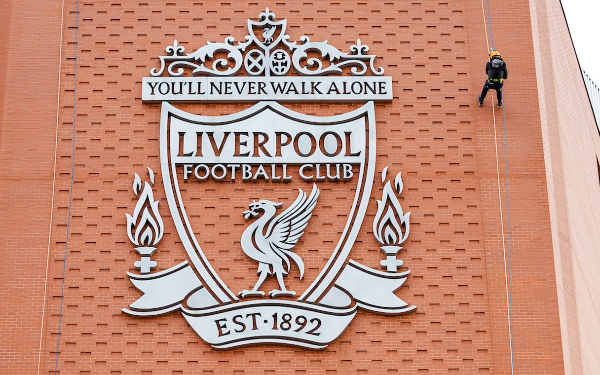 Person abseiling down Anfield Stadium wall with Liverpool FC crest.