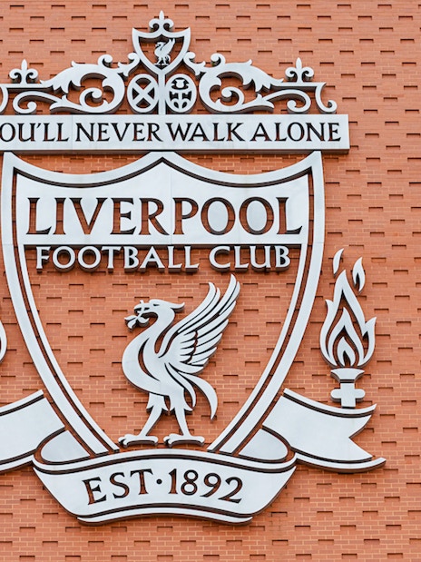 Person abseiling down Anfield Stadium wall with Liverpool FC crest.