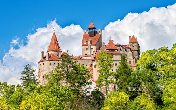 Bran Castle in Romania surrounded by lush green trees under a blue sky.