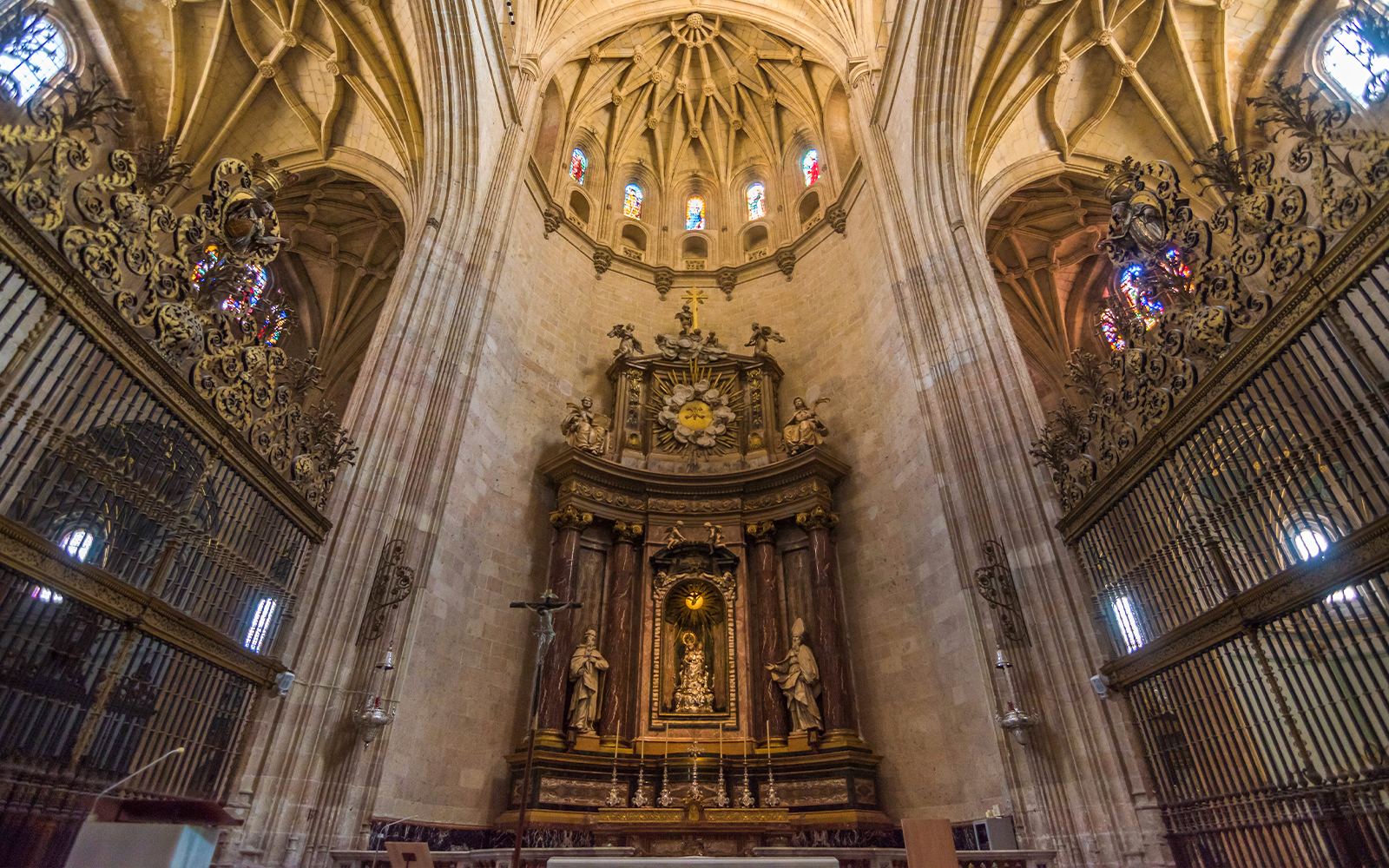 Main altar at the Cathedral of Segovia with ornate carvings and stained glass windows.