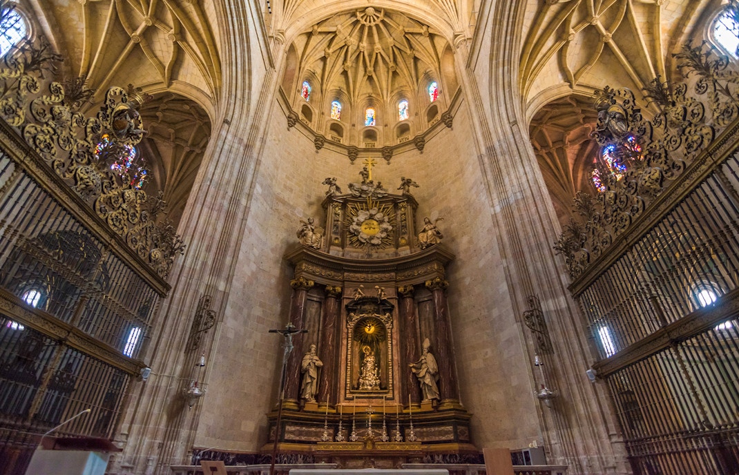 Main altar at the Cathedral of Segovia with ornate carvings and stained glass windows.