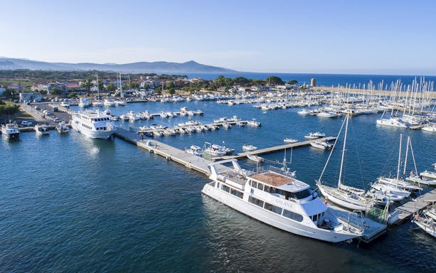 Deluxe boat docked at La Maddalena Archipelago marina, surrounded by yachts and scenic coastline.