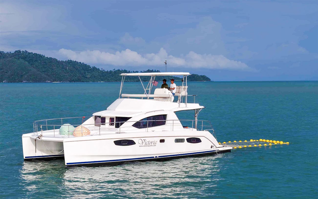 Victoria catamaran cruising at sunset near lush island, offering private Leopard tour experience.