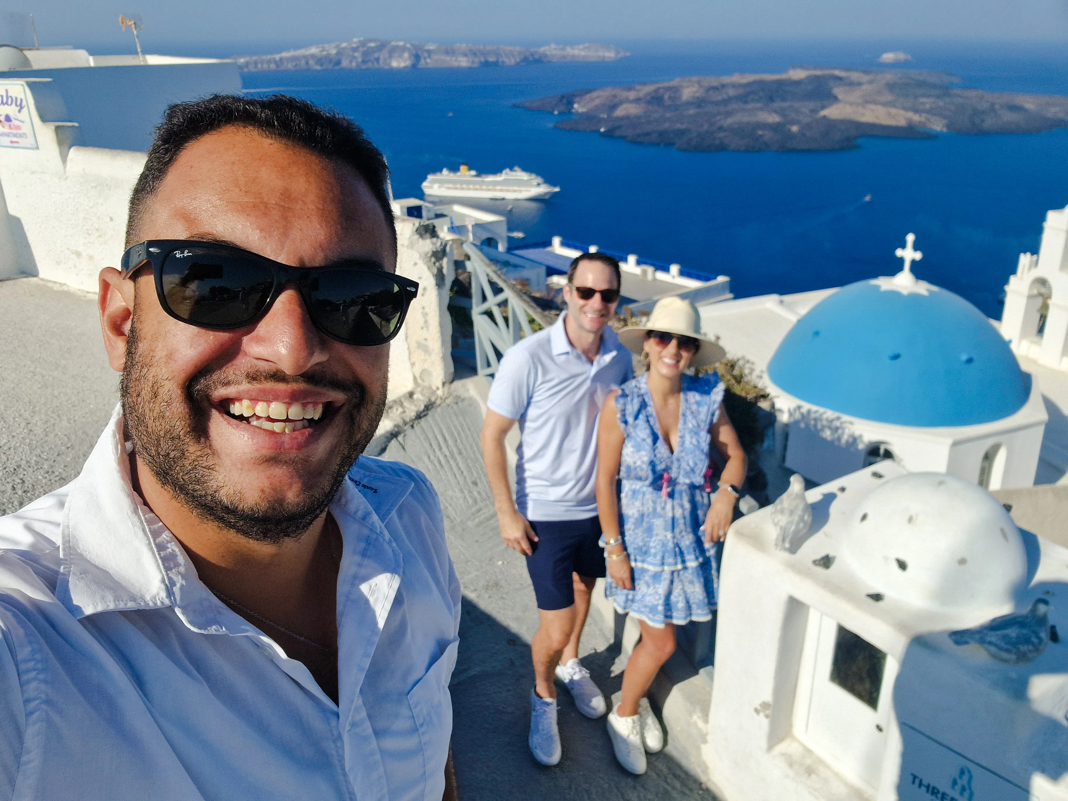 Tourists enjoying a view of Santorini's caldera with iconic blue domes and a cruise ship in the background.