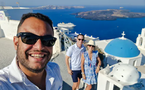 Tourists enjoying a view of Santorini's caldera with iconic blue domes and a cruise ship in the background.