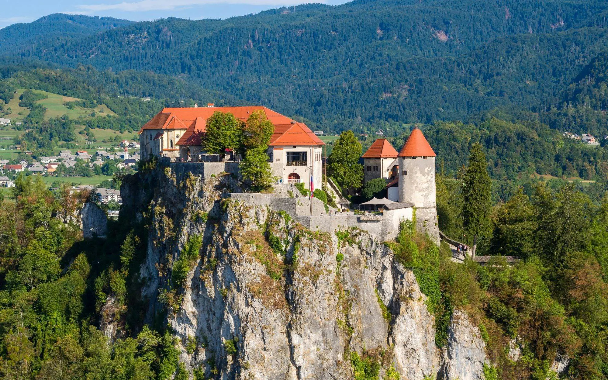 Bled Castle perched on a cliff with lush forest and mountains in Slovenia.