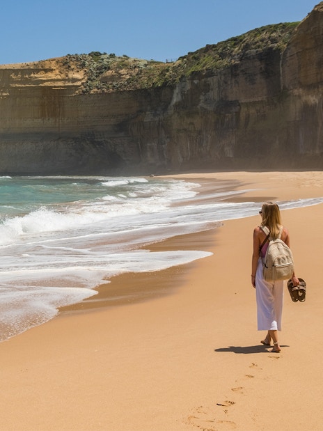 Person walking along a sandy beach with cliffs on the Great Ocean Road, Australia.