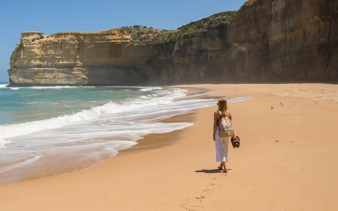 Person walking along a sandy beach with cliffs on the Great Ocean Road, Australia.