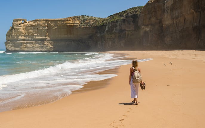Person walking along a sandy beach with cliffs on the Great Ocean Road, Australia.