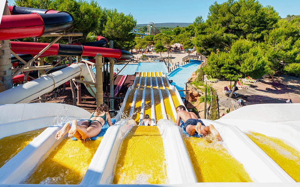 Riders on Crazy Horses water slide at Western Water Park, surrounded by trees and pools.