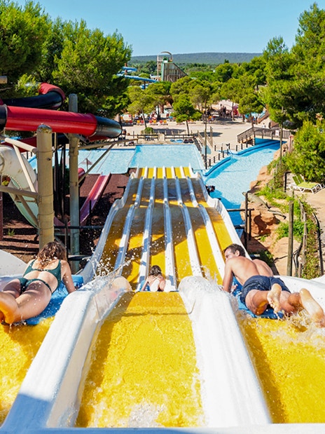 Riders on Crazy Horses water slide at Western Water Park, surrounded by trees and pools.