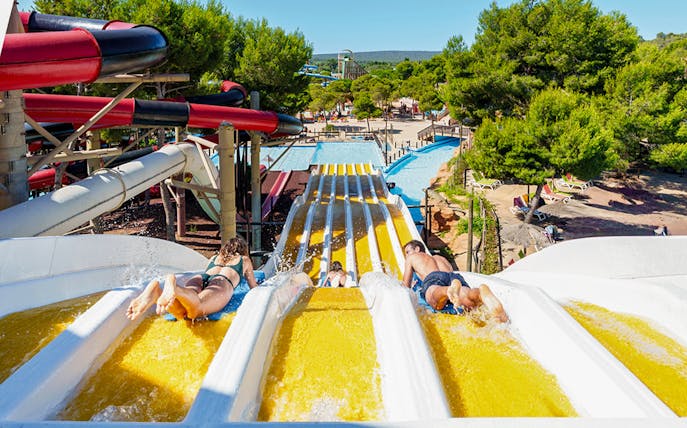 Riders on Crazy Horses water slide at Western Water Park, surrounded by trees and pools.