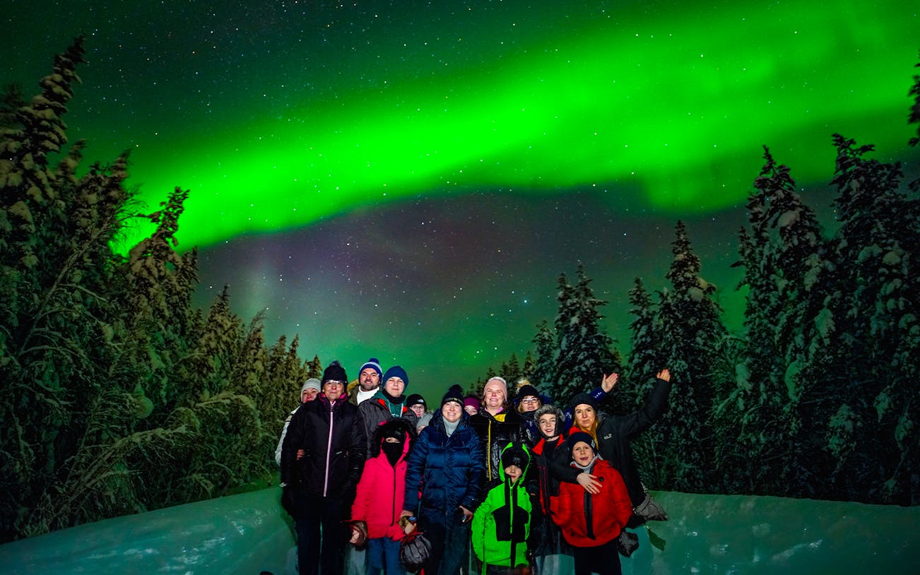 Group enjoying Northern Lights in snowy forest near Rovaniemi.