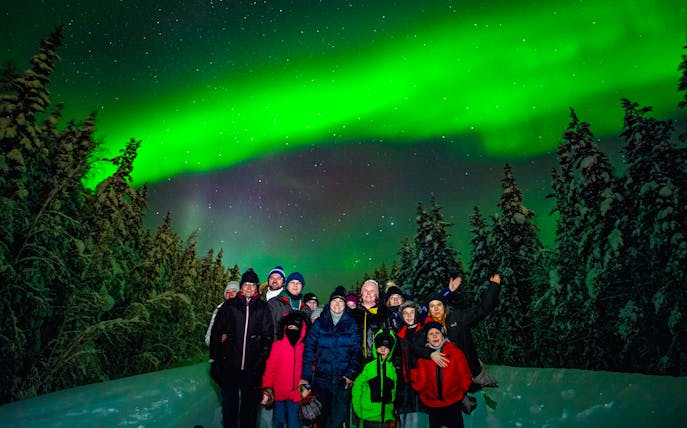Group enjoying Northern Lights in snowy forest near Rovaniemi.